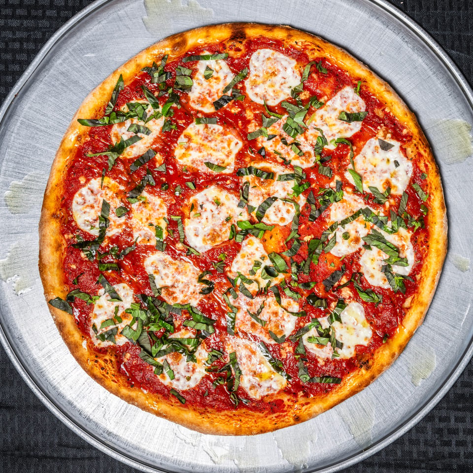 Margherita pizza with red sauce, mozzarella, and fresh basil on a metal pan.