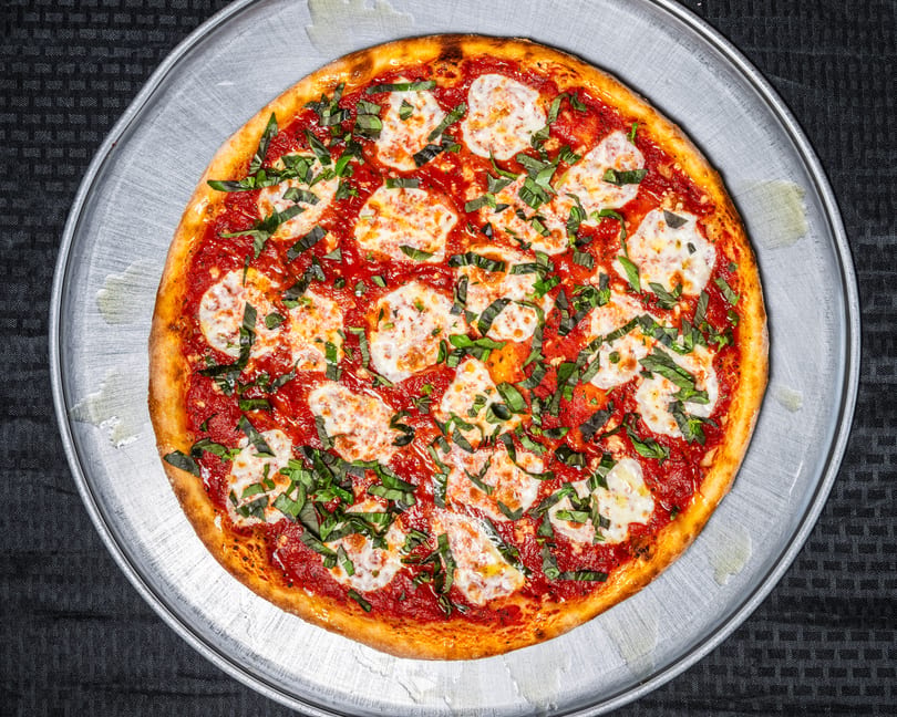 Margherita pizza with red sauce, mozzarella, and fresh basil on a metal pan.