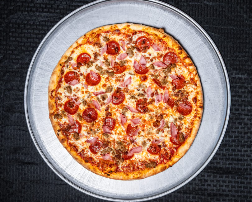 Whole meat lover's pizza with pepperoni, ham, and sausage on a metal pan.