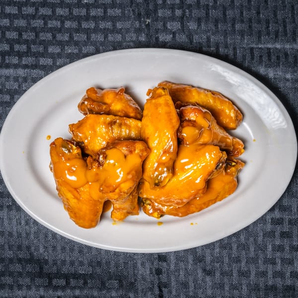 Golden-orange glazed chicken wings on a white oval plate.