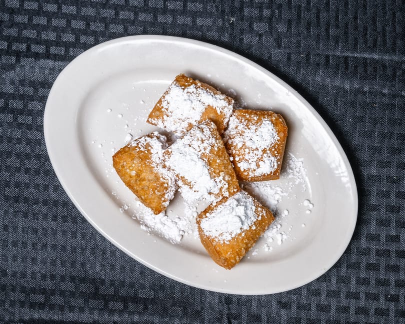 Golden-brown beignets generously dusted with powdered sugar on a white oval plate.