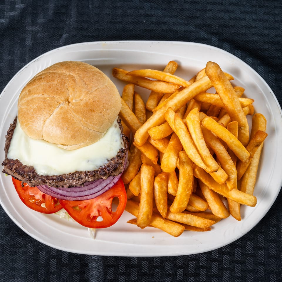 Cheeseburger with melted white cheese, tomato, and red onion, served with golden french fries on a white plate.