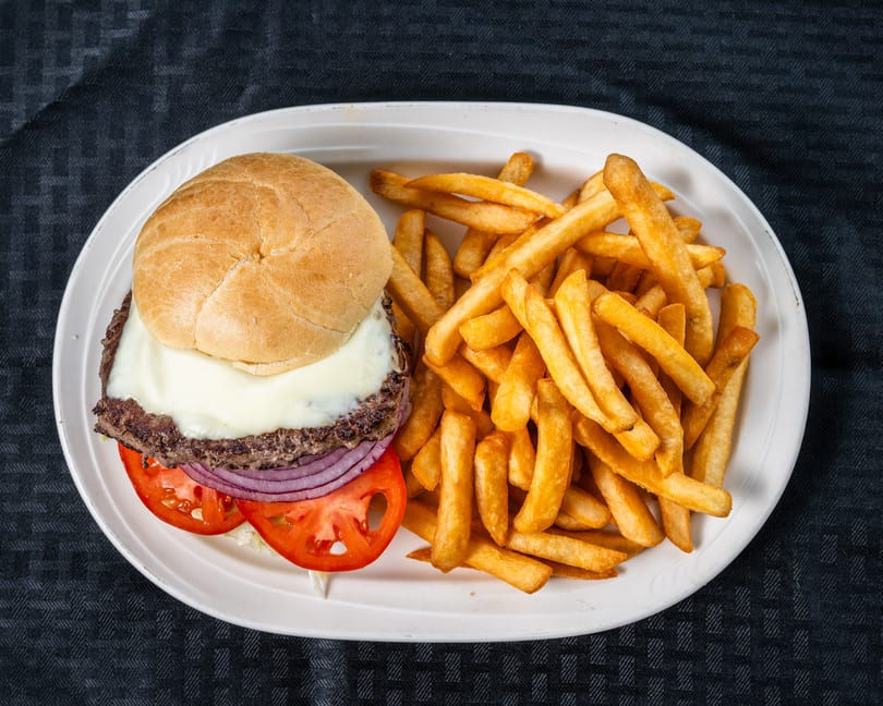 Cheeseburger with melted white cheese, tomato, and red onion, served with golden french fries on a white plate.