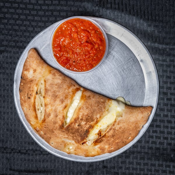 Calzone with melted cheese on a metal pan, served with a side of marinara sauce.