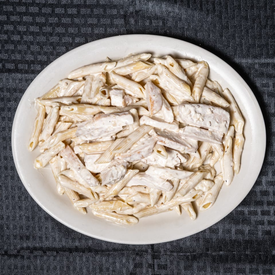Creamy penne pasta with chicken pieces served on a white plate.