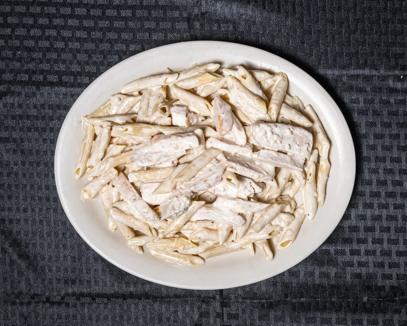 Creamy penne pasta with chicken pieces served on a white plate.