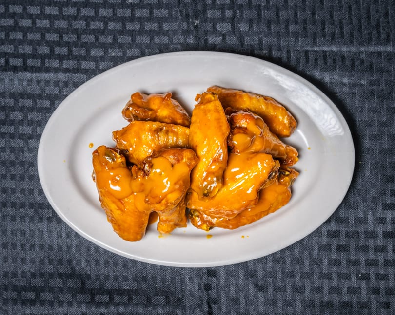 Golden-orange glazed chicken wings on a white oval plate, on a dark gray patterned tablecloth.