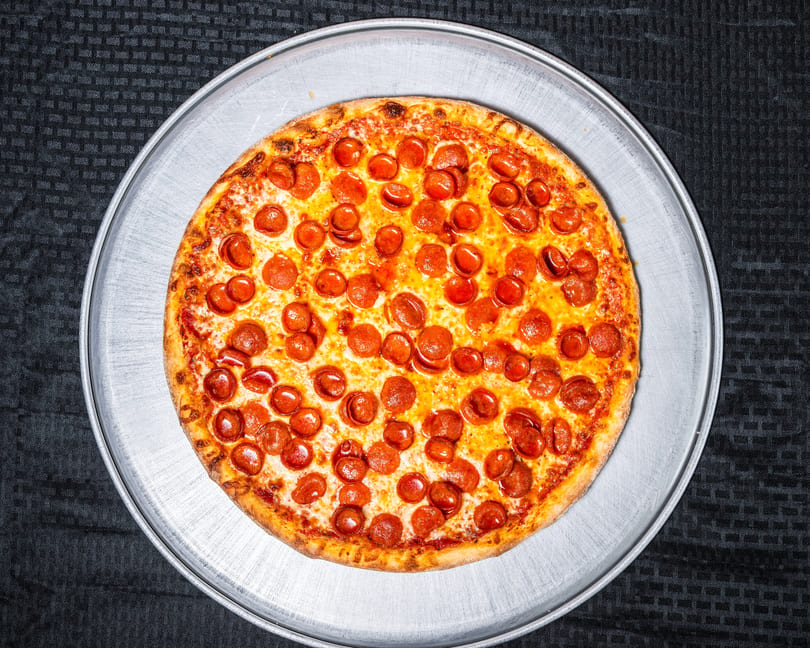 A large, hot pepperoni pizza sits on a round metal serving tray.