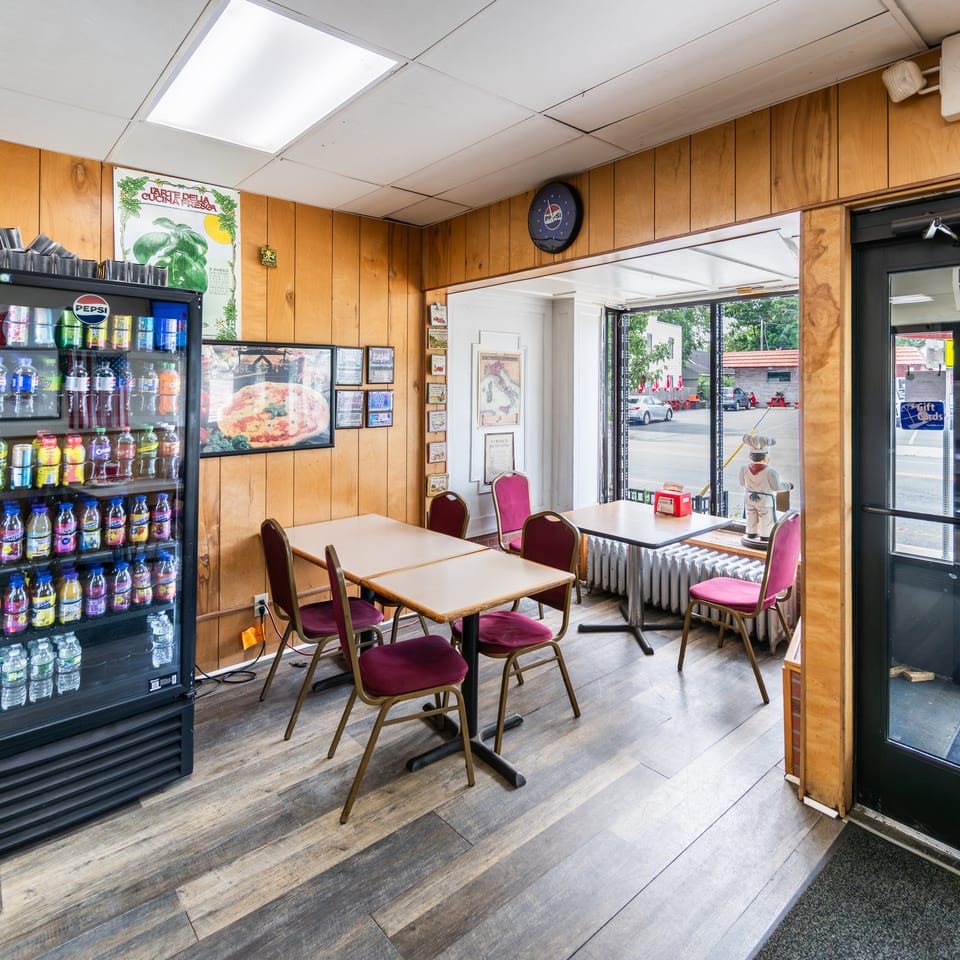 Casual restaurant interior with wood-paneled walls, tables, maroon chairs, a drink cooler, and a street view.
