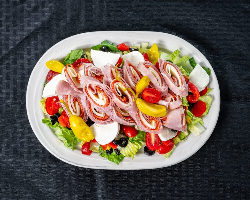 Colorful antipasto salad featuring rolled deli meats, fresh mozzarella, cherry tomatoes, olives, and yellow peppers.