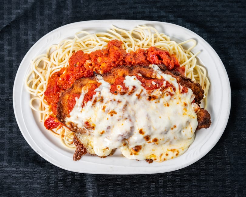 Spaghetti with chicken parmesan covered in melted cheese and red sauce on a white plate.