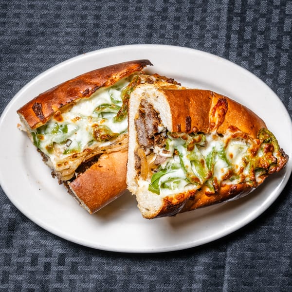 Two halves of a toasted sub sandwich filled with steak, onions, green peppers, and melted cheese.