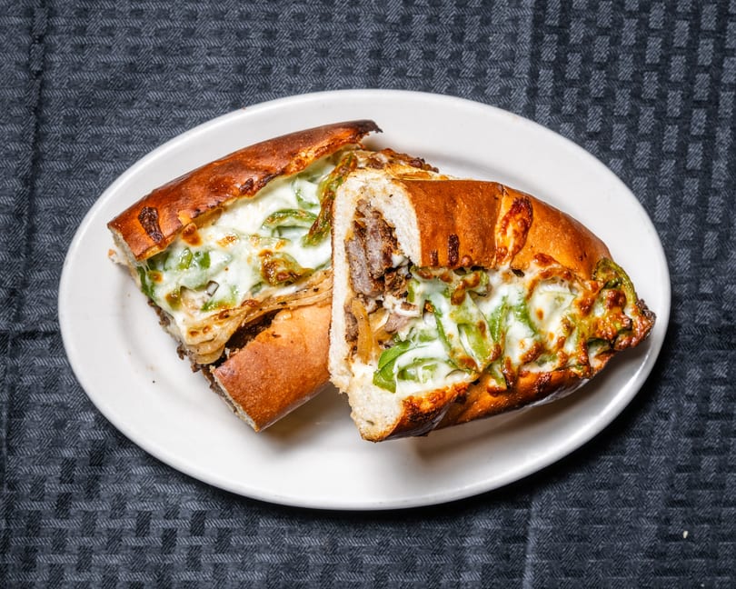 Two halves of a toasted sub sandwich filled with steak, onions, green peppers, and melted cheese.