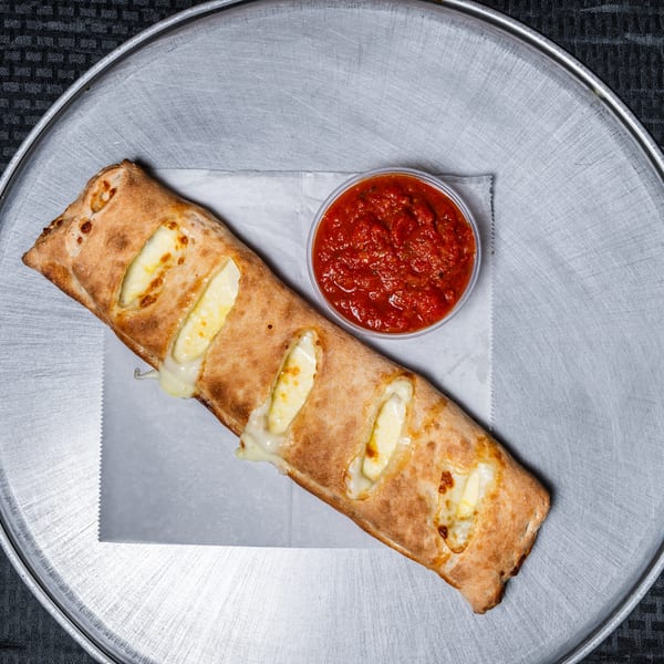 Golden-brown calzone with melted cheese and a side of marinara on a metal pan.