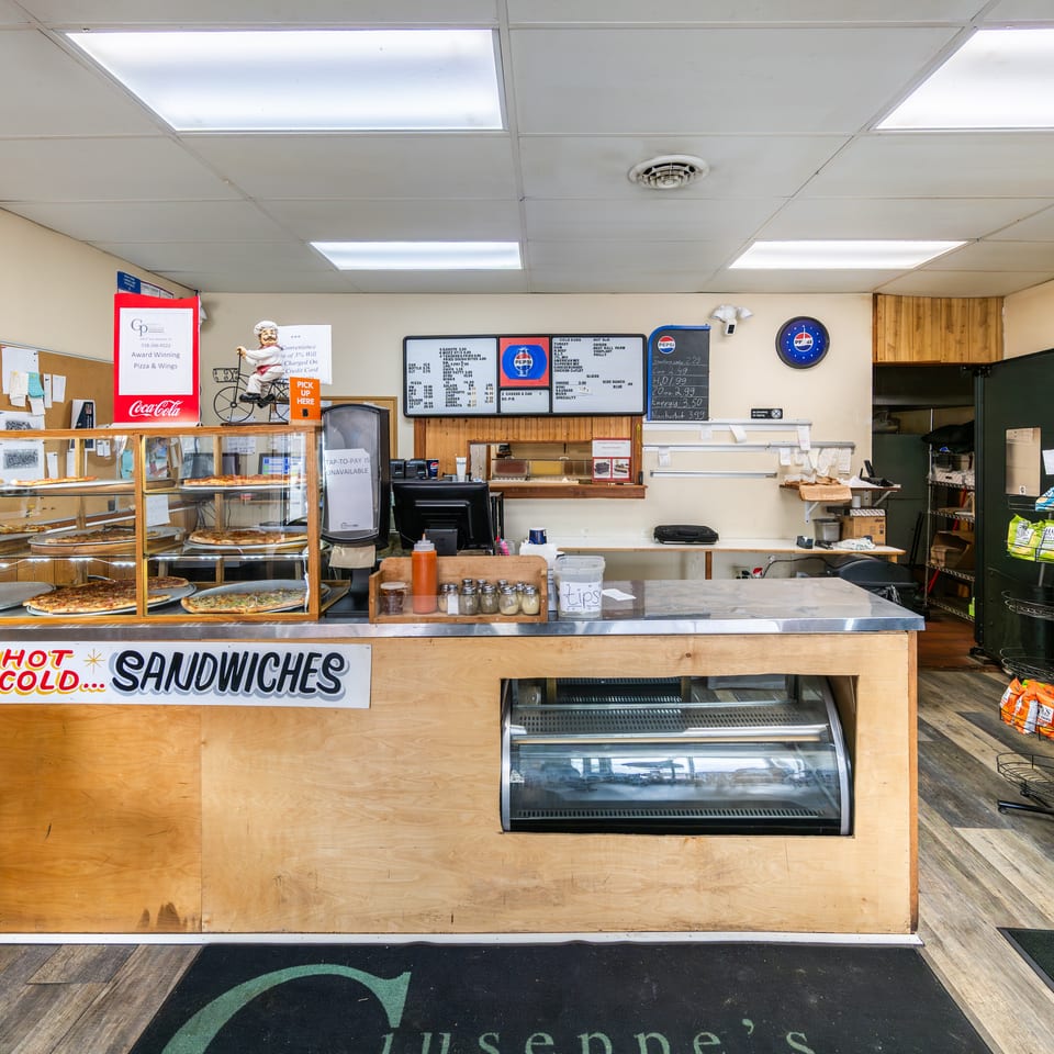Counter at Giuseppe's pizza and sandwich shop with pizzas in a display case and menu.