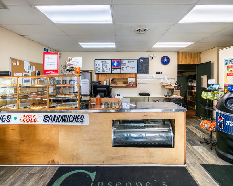 Counter at Giuseppe's pizza and sandwich shop with pizzas in a display case and menu.