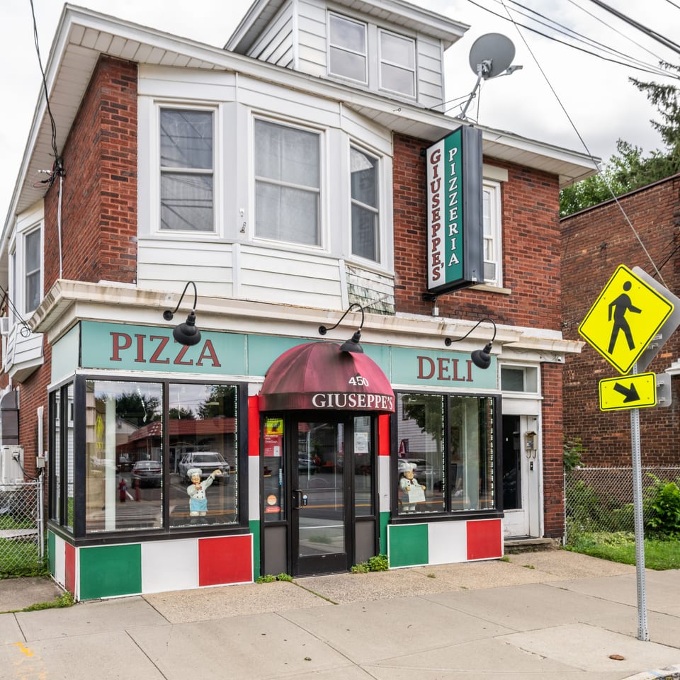 Giuseppe's Pizzeria and Deli building with a red awning, chef statues, and Italian flag colors.