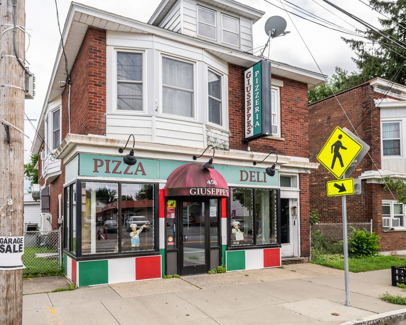 Giuseppe's Pizzeria and Deli building with a red awning, chef statues, and Italian flag colors.