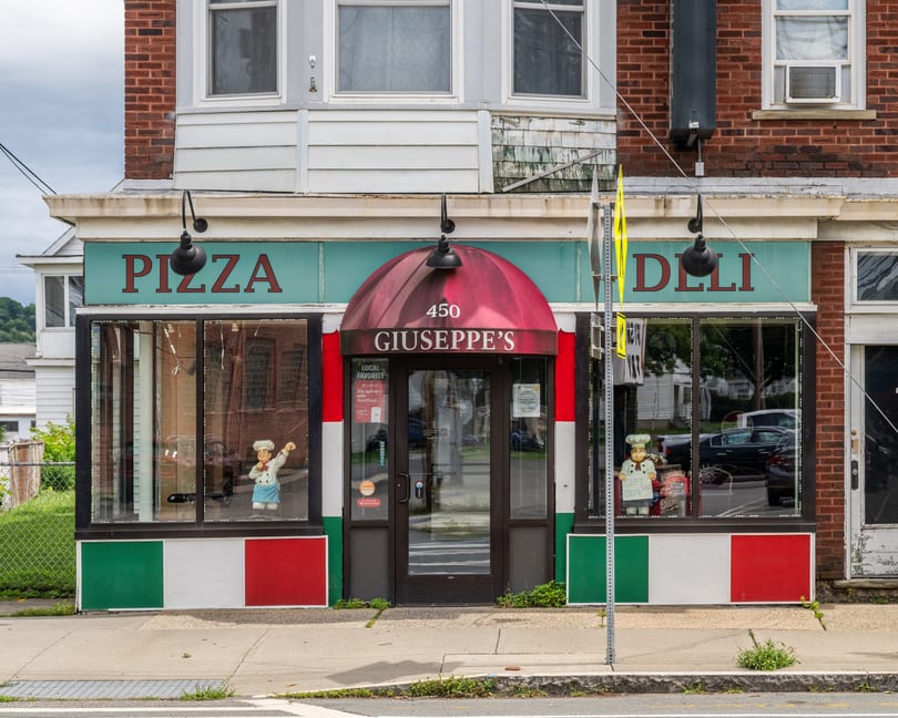 Giuseppe's Pizza and Deli storefront with red awning, Italian flag colors, and chef statues.