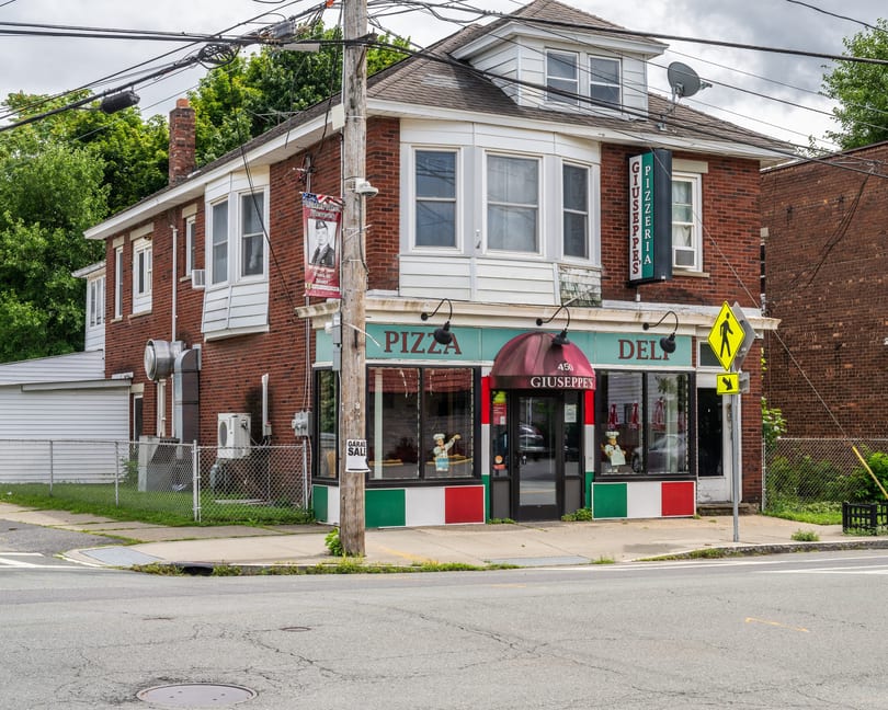 Giuseppe's Pizzeria & Deli on a street corner, with Italian flag colors on its facade.
